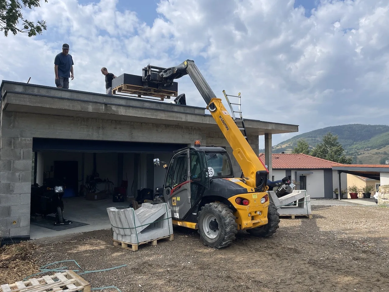 Deux installateurs de C.E.L Clim'Elec montant des panneaux photovoltaïques sur un toit à l'aide d'un chariot télescopique