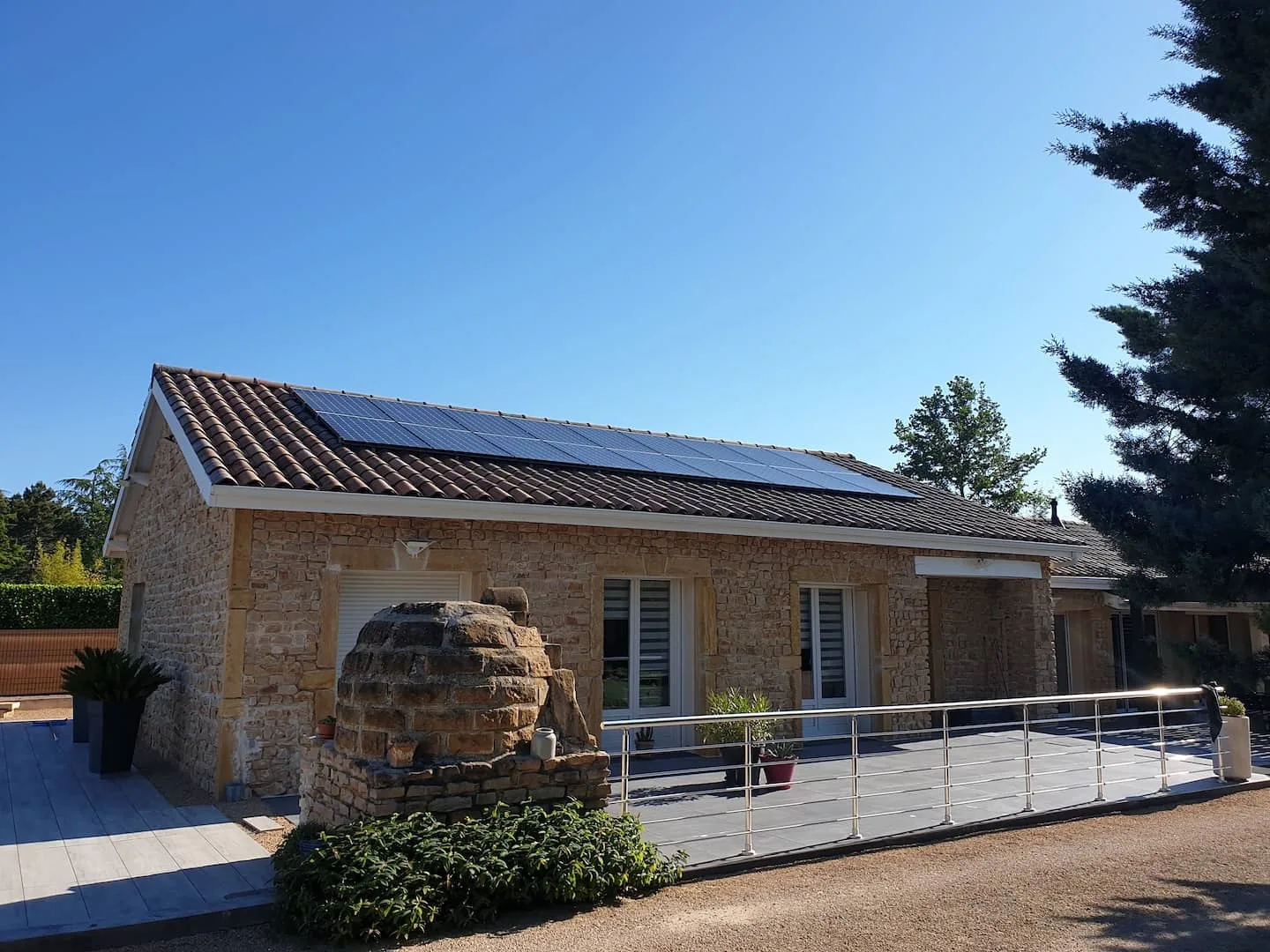 Panneaux photovoltaïques posés par C.E.L Clim'Elec sur la toiture en tuiles d'une maison en pierre, sous un grand ciel bleu