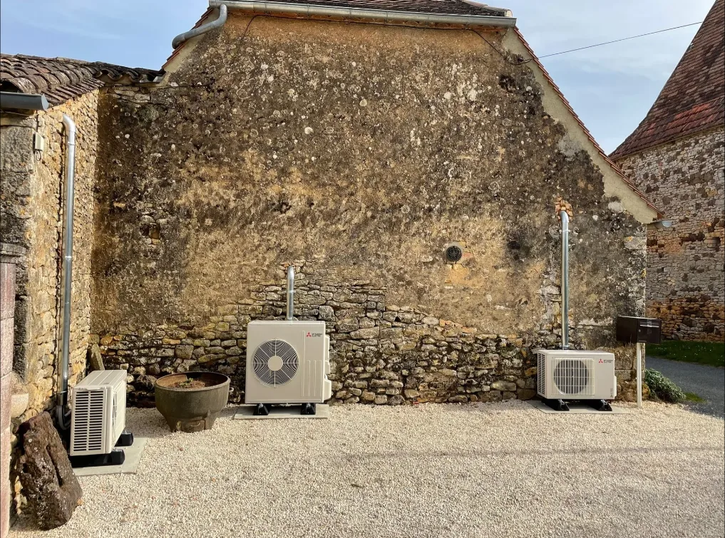 Unités extérieures de climatisation posées au pied d'un mur en pierre ancienne